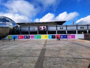 Colourful Open Summer hoarding graphics running across a large public square