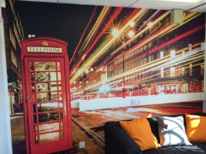 Wall mural of a red telephone box and London light trails behind a sofa